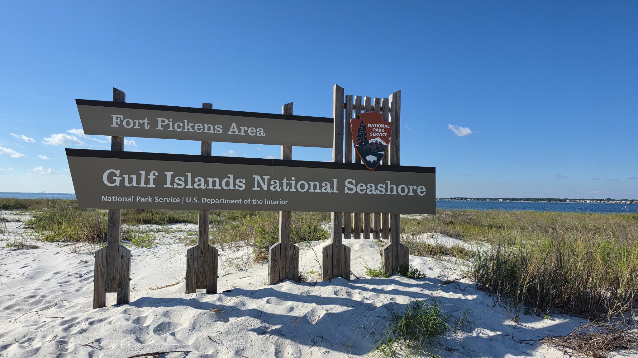 Fort Pickens entrance sign beside the white sand and water of Gulf Islands National Seashore